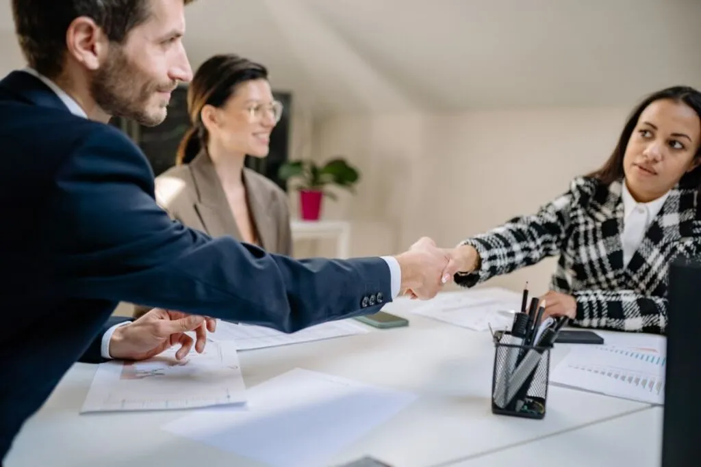 Executivo e cliente realizando aperto de mão após apresentação de proposta comercial com documentos visíveis sobre a mesa em reunião de negócios