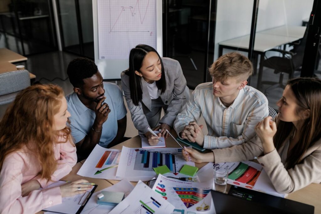 Equipe comercial B2B diversa discutindo estratégia de prospecção e social selling com gráficos e dados sobre a mesa em reunião de planejamento