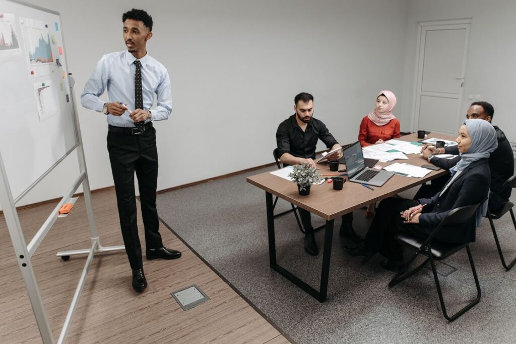 Profissional apresentando estratégia comercial no quadro branco com gráficos para equipe diversa em reunião de metodologia de vendas B2B no escritório