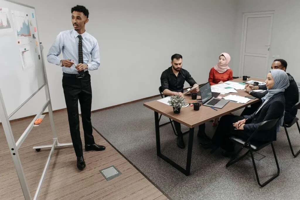 Profissional apresentando estratégia comercial no quadro branco com gráficos para equipe diversa em reunião de metodologia de vendas B2B no escritório