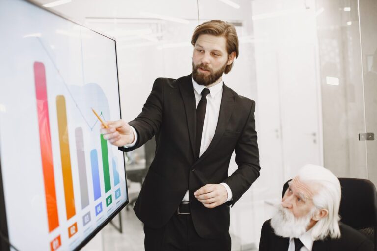 Vendedor de terno apontando dados de crescimento em tela para executivo sênior durante apresentação de proposta comercial B2B
