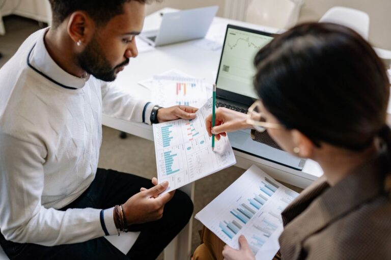 Dois profissionais revisando gráficos de desempenho comercial em relatórios impressos no escritório