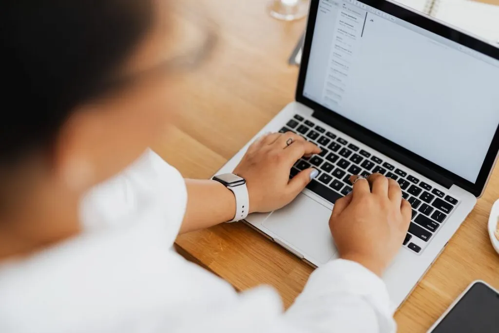 Pessoa escrevendo um e-mail no laptop em uma mesa de madeira