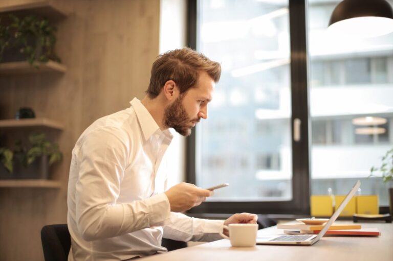 Executivo à mesa do escritório conferindo o celular enquanto espera retorno de um cliente