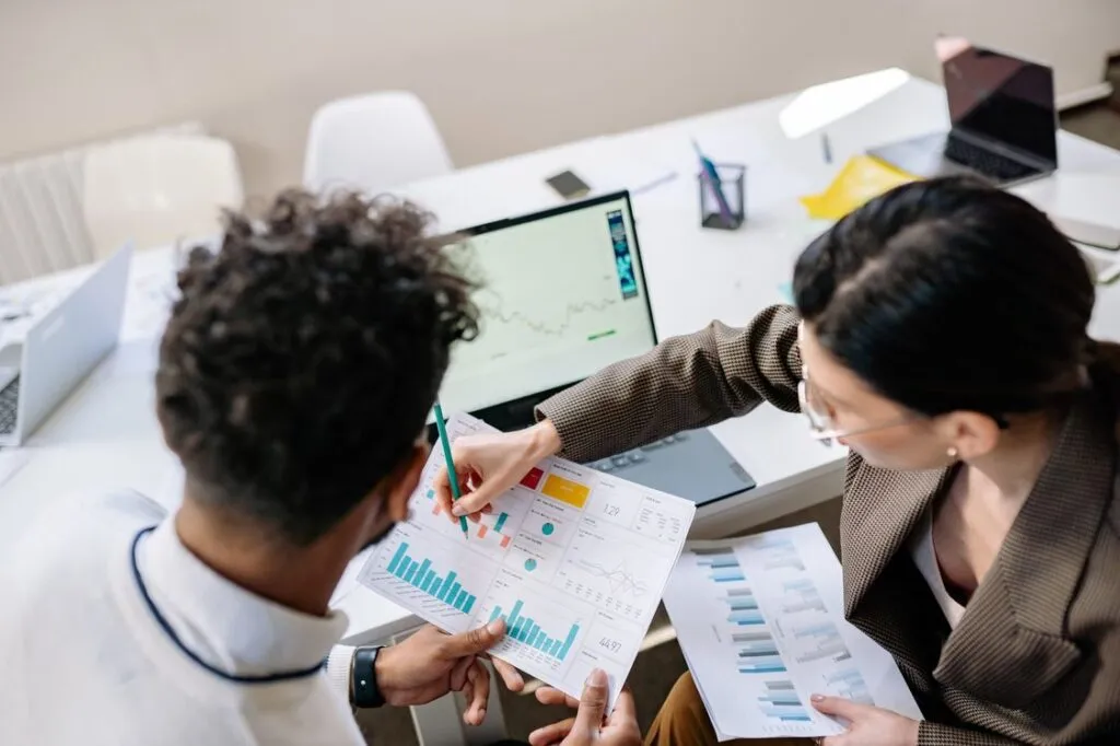 Dois profissionais analisando gráficos de mercado no papel e no laptop