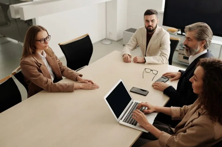 Quatro profissionais em reunião ao redor de uma mesa, com um notebook aberto